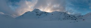 A panorama taken from the bowl of the Ring of Steall at dusk. The sky is still bright with dramatic clouds, but the mountains and ground around are getting dark.
