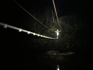 Chris crossing a rope bridge over a river, coming towards the camera. It’s pitch black, and he’s got a headtorch to lead the way.