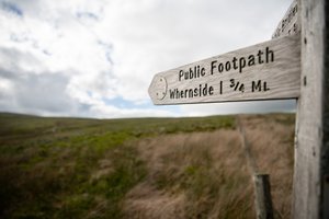 A footpath sign points from right to left, marking the summit of Whernside, 1.75 miles away.