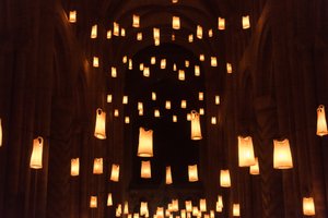 The vast hall of Durham Cathedral at night. The hall is filled at various levels by warm hanging lights. On closer inspection, the lights are made from white vests lit from within.