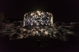 A large cylindrical light projects abstract patterns outwards on to the surrounding walls