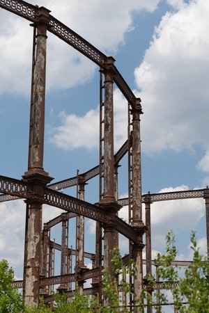 A portrait photo of the side of a gas works, with another visible in the distance. The metal is mostly rusted with patches of peeling paint visible.