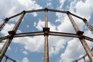 Looking straight up at the side of a gas works from close by. The metal railings are rusted with peeling paint.