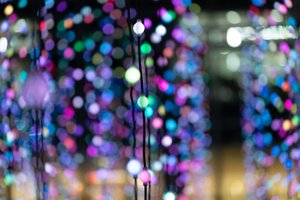 A lighting installation with thousands of coloured lights. The room is filled with strings of round ball-shaped lights hung from the ceiling. The image is focussed on as ingle strand with three ball lights visible - and many thousands of coloured lights blurred behind.