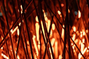 A close crop of a lighting installation made from thousands of short light sticks. Each light stick rhythmically glows orange. In the close crop, some sticks are unlit and the overall image has the appearance of fire.