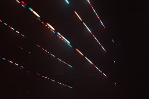 Multicoloured lines of light in a dark room converge to the bottom right.
