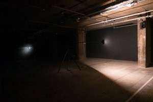 In a dark room, a light in the middle faces to the right and has illuminated one half. What can be seen is bare concrete.