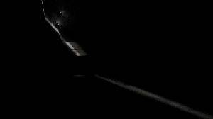Video showing three pendulums suspended from a high ceiling in a dark room. They are swinging left and right and have faint lights on them.