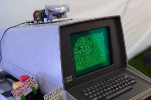 A vintage computer with glowing green display shows a pattern on screen.