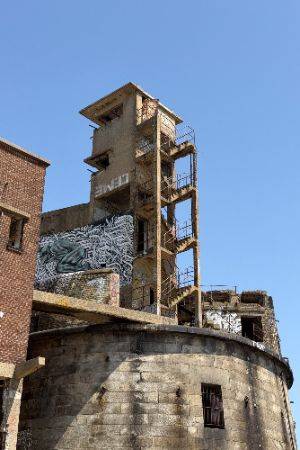 Exterior photo looking up a decaying concrete staircase attached to a narrow tower.