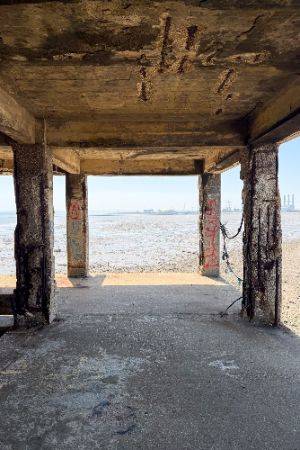 Photo looking straight on to some decaying concrete columns and then muddy estuary beyond.