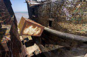 Exterior photo taken from on top of the battery, showing a large rectangular metal object precariously wedged between two buildings.