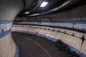 A curved underground tunnel with cream and light blue tiles