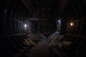 Looking straight on inside wide tunnel with metal walls and debris on the floor