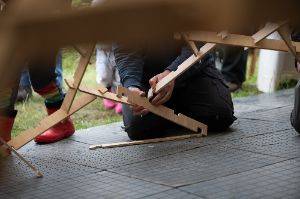 A person kneels down to connect two wooden slats of a large dome together