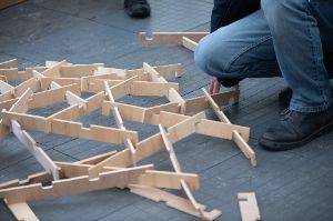 A person kneels next to a bunch of wooden slats connected together in a lattice