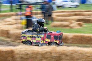 Person driving a go-kart in the shape of a fire truck amongst hay bales as part of Wacky racers.