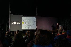 Photo of a projection screen in front of an audience. The slide has the word “Chicken:” to the left of a flow diagram about chicken.