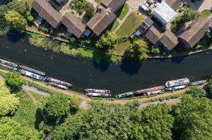 A drone photo of a canal. The camera is facing straight down. There are canalboats on one side.