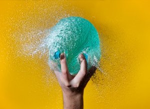 Photo of a pale blue waterballoon bursting in a hand.