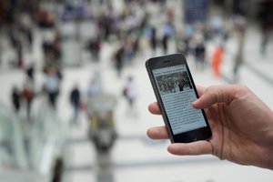 Photo of a hand holding a smartphone, which is showing a web article.