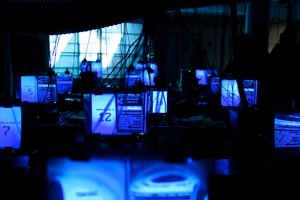 A dark mysterious photo showing several computer screens lit up with magnifying panels in front of them.